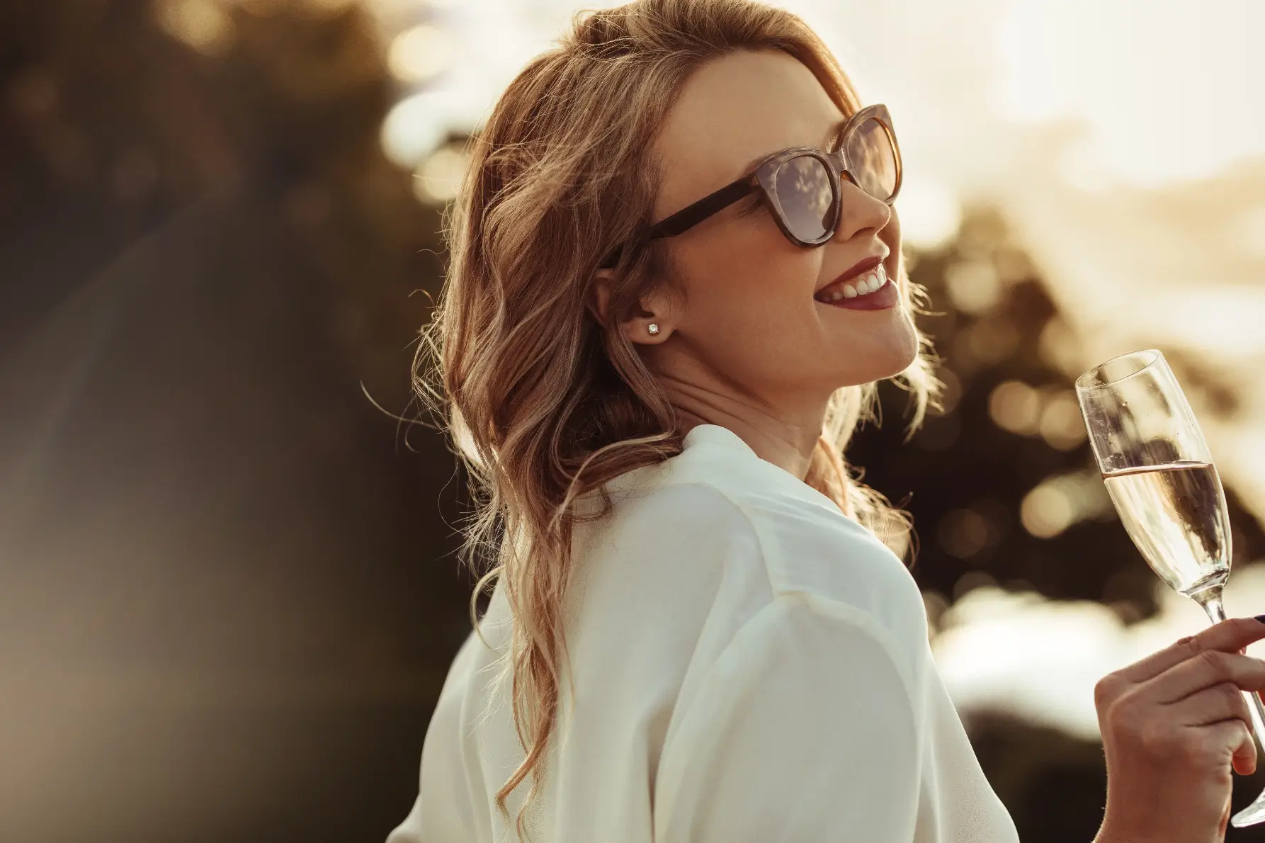 A woman in sunglasses holds a glass of champagne.