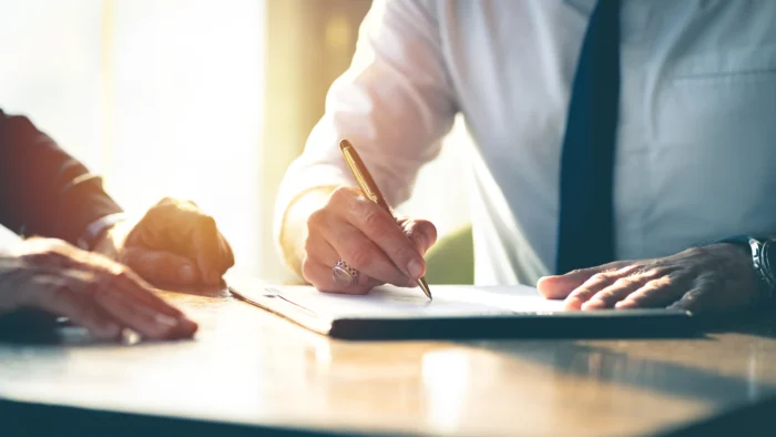 Two people sit at a table signing a document.
