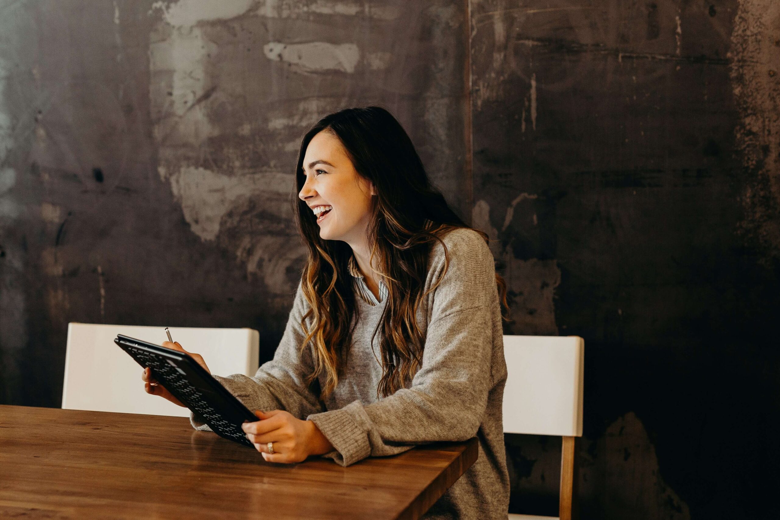 A woman laughing sits at a table holding a laptop.