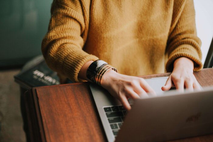 A person in a yellow jumper works at a table with a laptop on it.