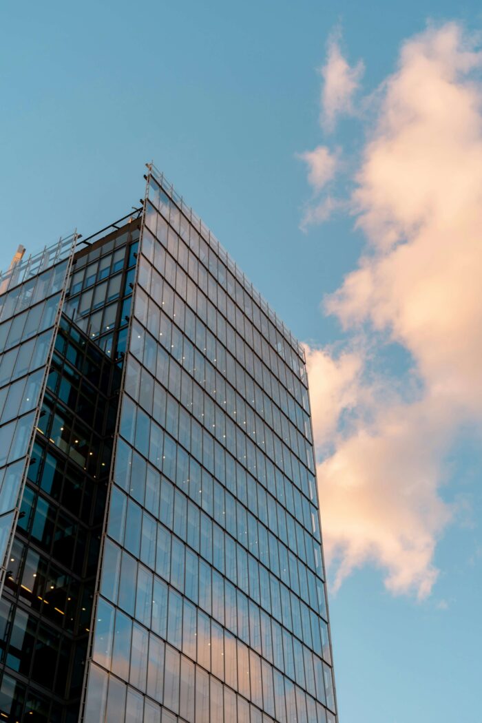 A glass fronted skyscraper is pictures against and blue sky with clouds.