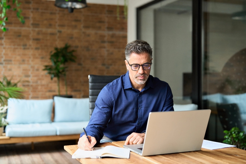 Man taking notes while working on a laptop